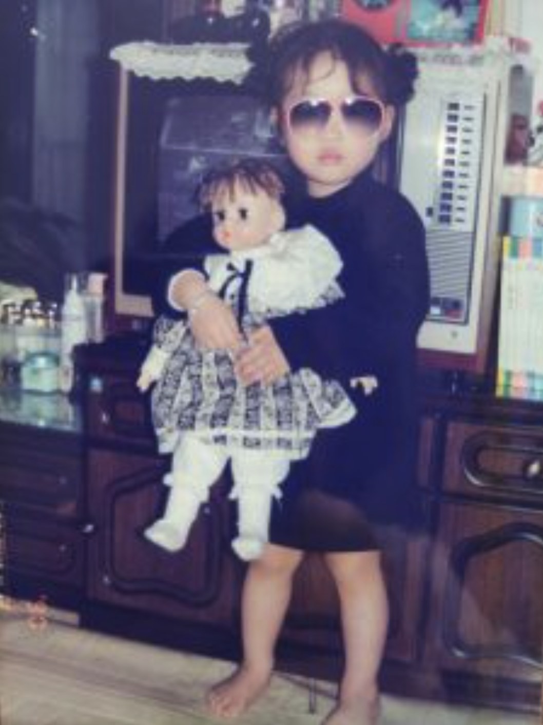 Inyoung as a toddler in sunglasses, holding a doll